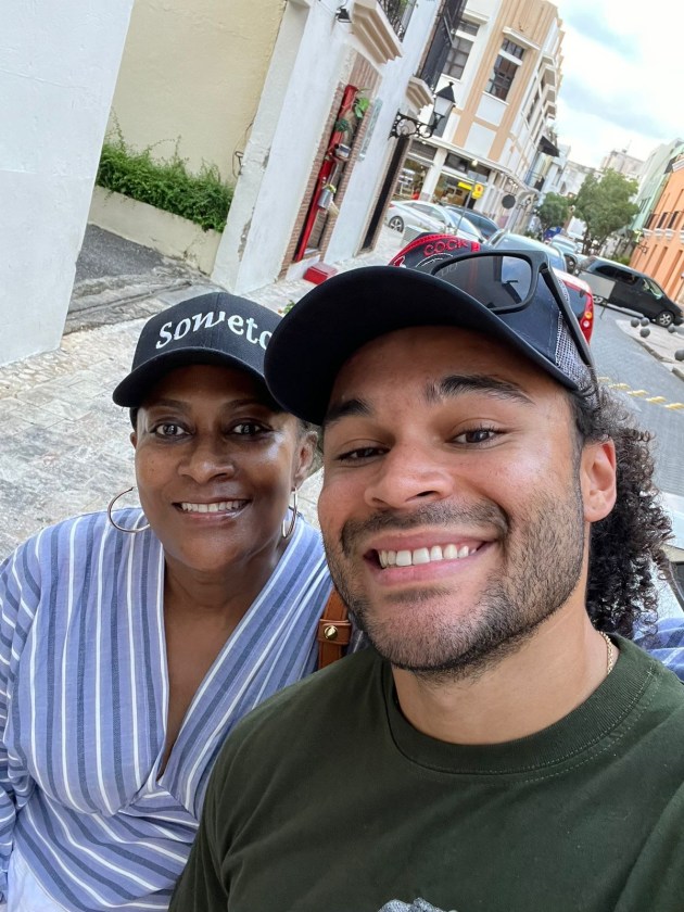 A woman and man, both wearing black baseball caps, pose for a selfie while standing on a sidewalk