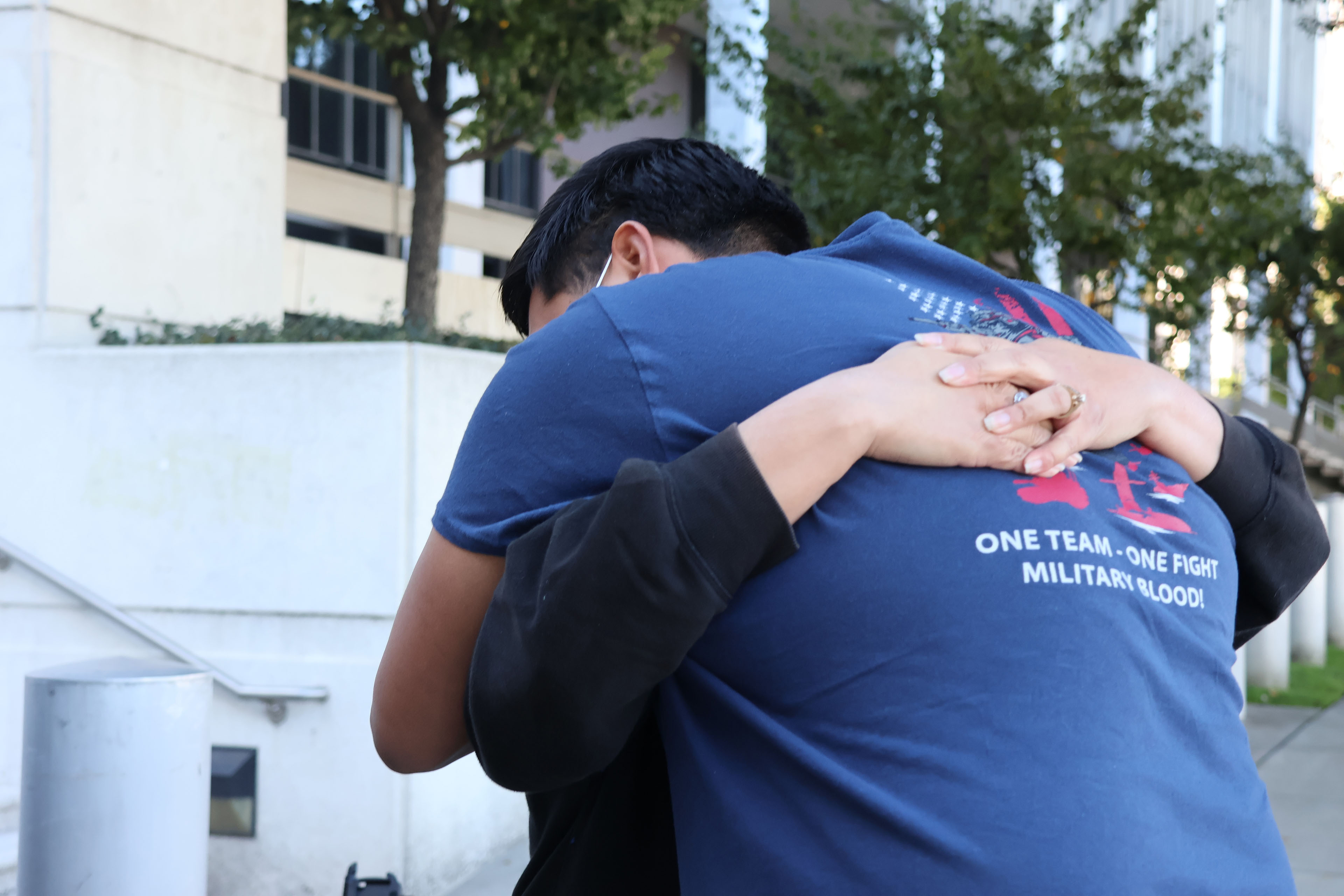 A young man leans down to hug a woman. Neither of their faces are visible to the camera.